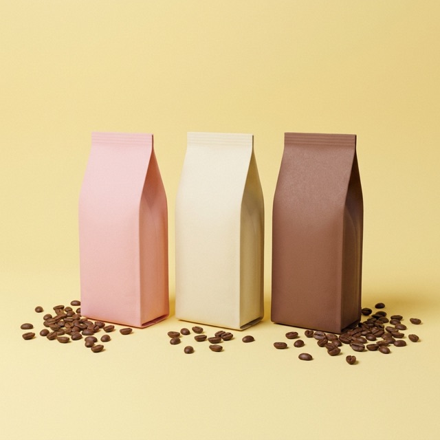 Three pastel coffee bags in pink, cream, and cocoa standing in a row